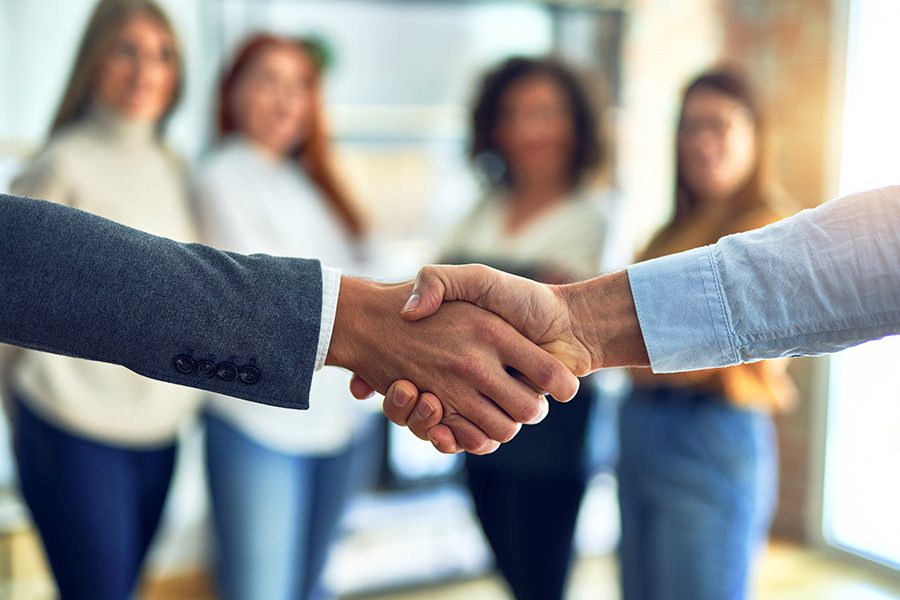 About Our Agency - Family-Stark Insurance Agency Team Members Shaking Hand After a Successful Business Meeting With Coworkers Looking on in the Background