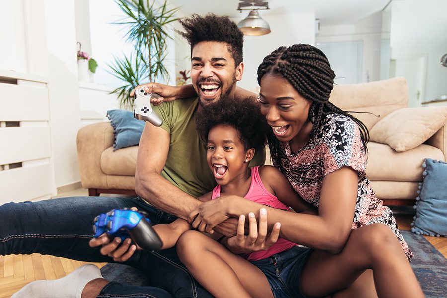 Personal Insurance - Smiling Happy Family Having Fun While Sitting on the Floor in Front of Couch Playing Video Games Together